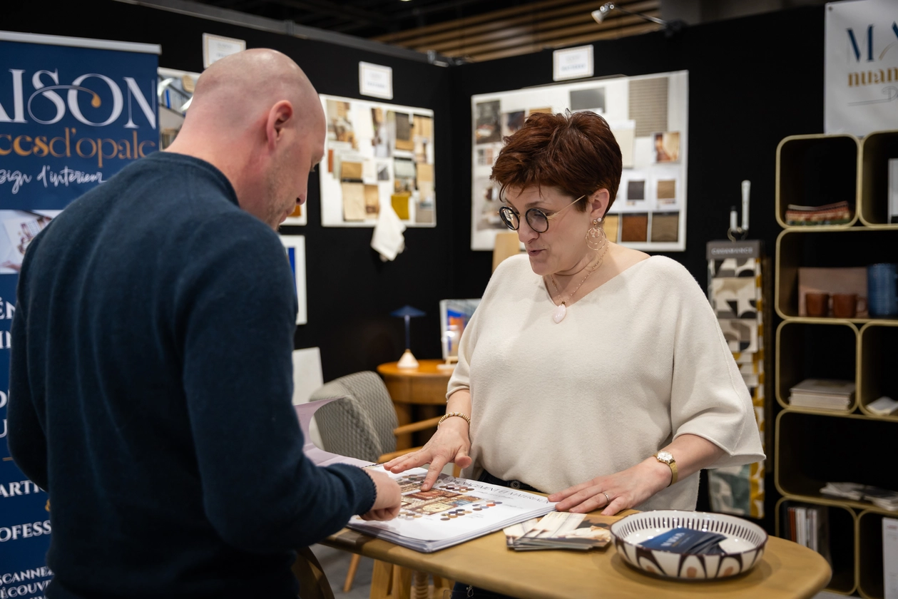 Une exposante montre quelque chose à un visiteur sur une documentation commerciale